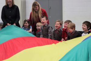 Children smiling as they pull the parachute up and down