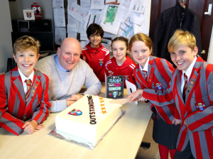 Ghyll Royd children smiling around a cake that says 'Outstanding' on the front.